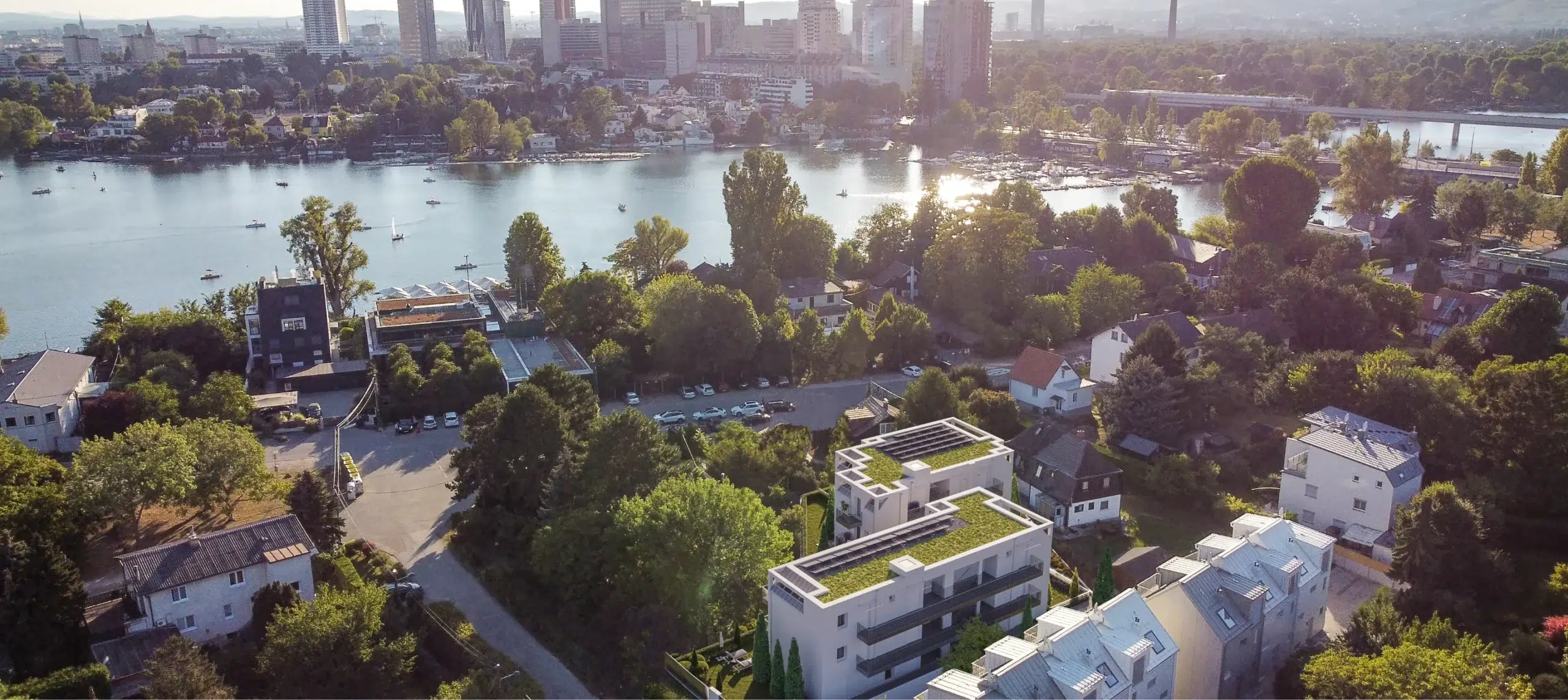 Luftbild der Alten Donau mit Blick auf das Projekt AG3, eingebettet in grüne Umgebung und mit Blick auf die Skyline von Wien.