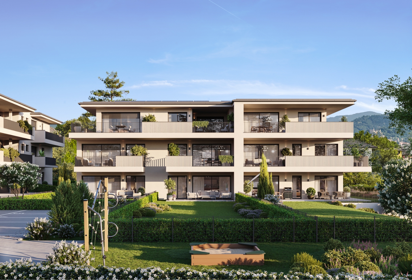 Modernes Wohngebäude mit großzügigen Balkonen, Grünflächen und Spielplatzbereich vor einer hügeligen Landschaft.